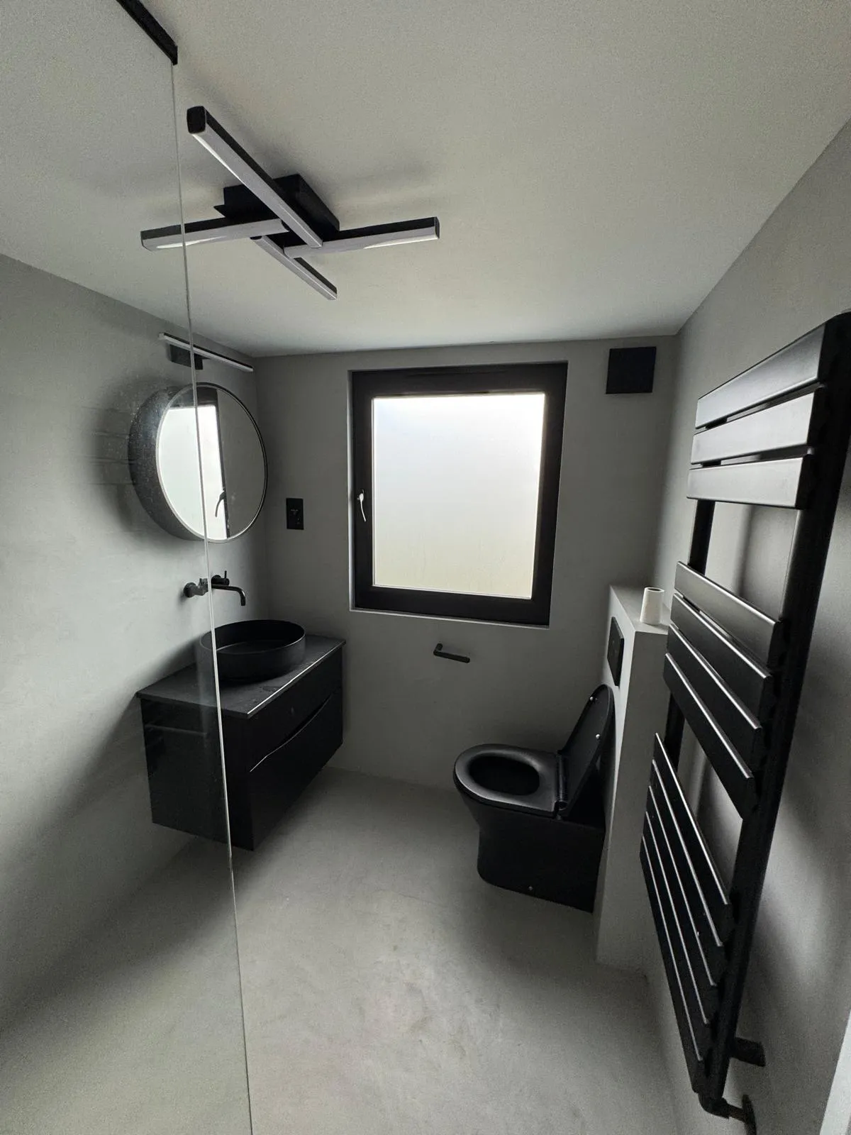 Finished compact shower room with microcement walls, matte black basin and fittings, round mirror and black towel radiator