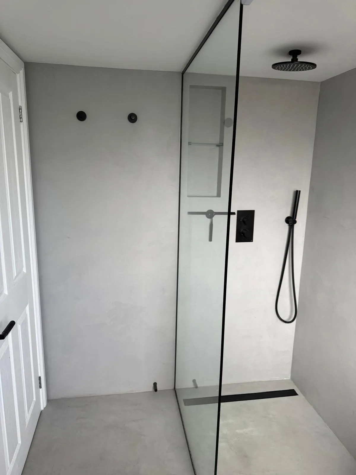 Finished walk-in shower with microcement walls, frameless glass panel, matte black controls and ceiling rain head