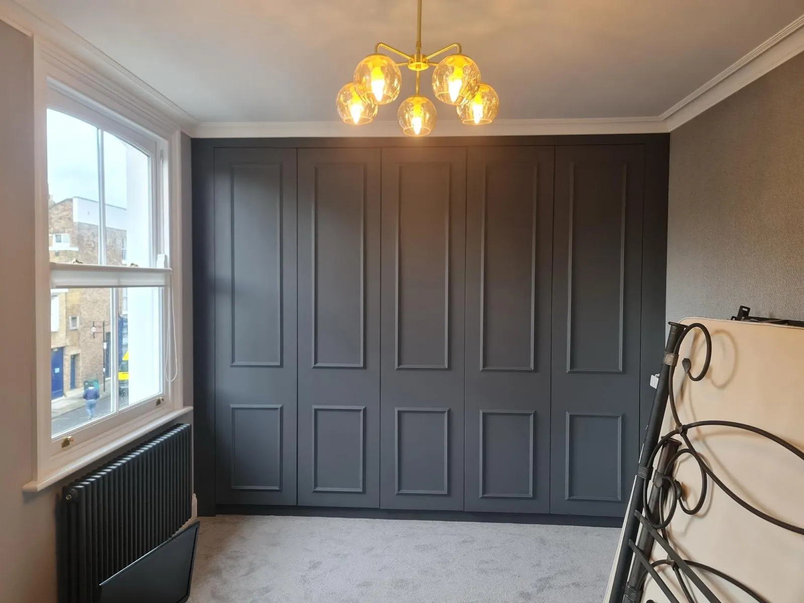 Finished bedroom with full-wall graphite-grey fitted wardrobe, raised panel doors, brass handles and globe pendant chandelier
