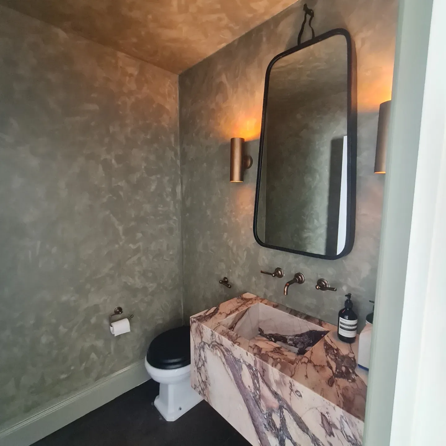 Cloakroom with Venetian plaster walls, book-matched marble trough sink, brass taps and leather-strap mirror