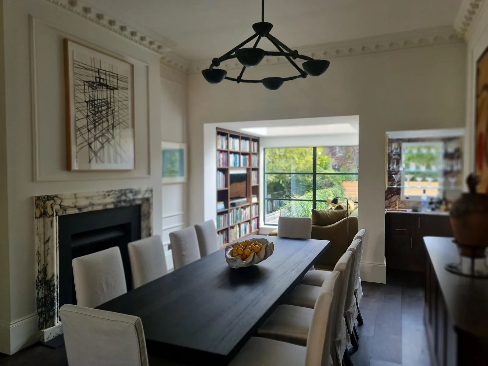 Finished dining room with dark oak table, marble fireplace, sculptural black chandelier and view to garden-facing library extension