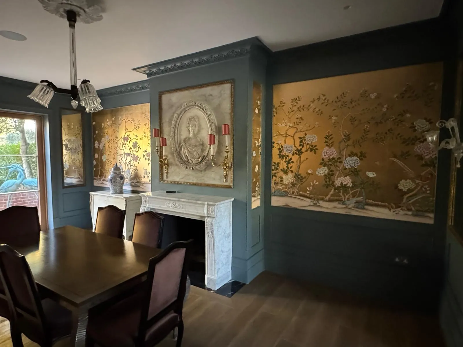 Finished dining room with sage-blue panelling, marble fireplace, chinoiserie panels, bas-relief medallion and crystal chandelier