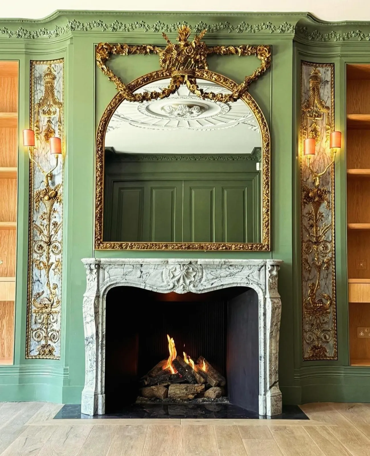 Grand Rococo marble fireplace with open fire, set in green panelled walls with gilt overmantel mirror and decorative pilasters