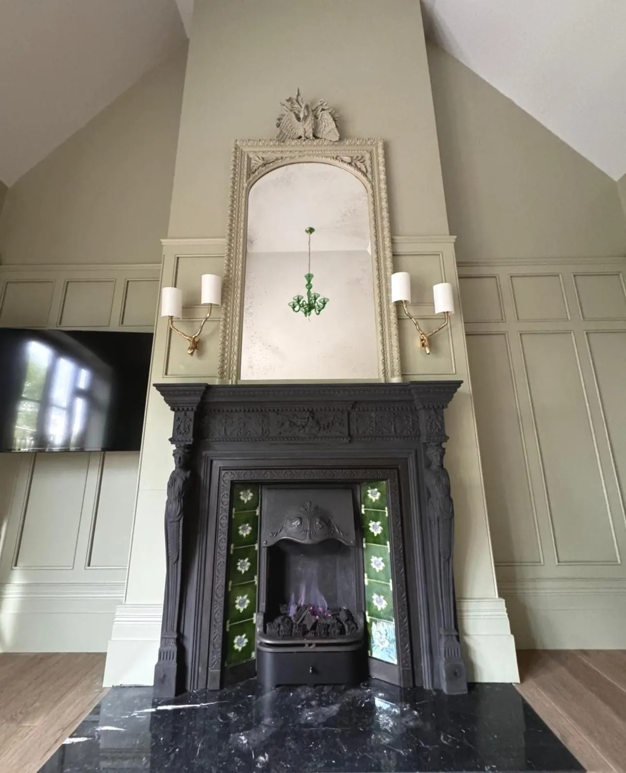 Victorian black cast-iron fireplace with green tile insert and arched cream overmantel mirror in sage-green panelled room