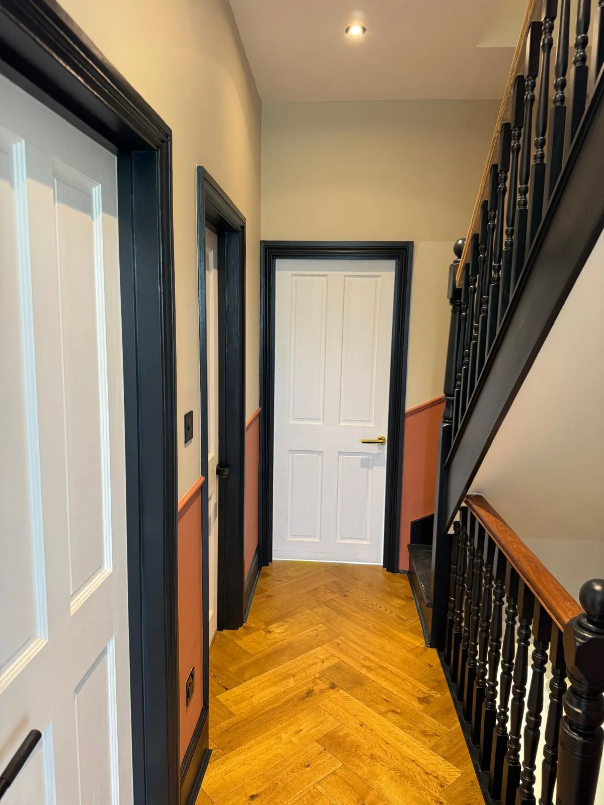 Finished hallway with herringbone oak parquet floor, terracotta and white two-tone walls, black stair balustrade and white panel doors