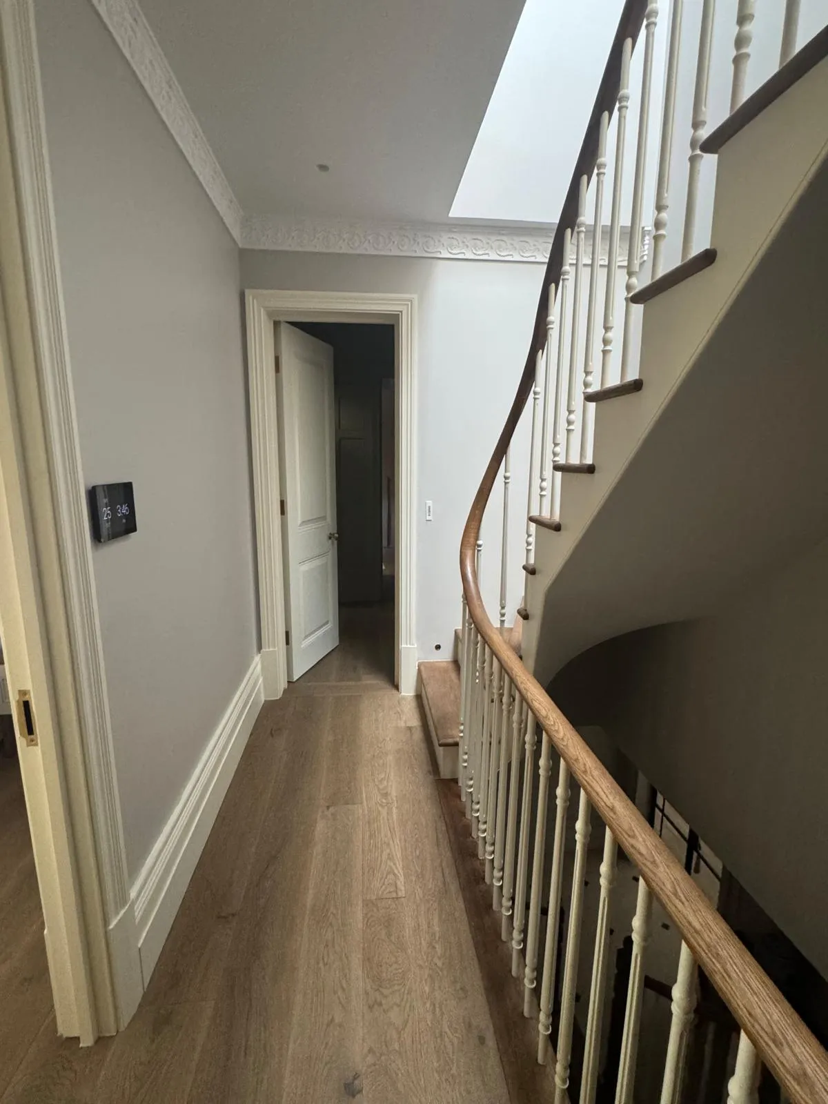 Finished landing with grey-beige walls, dentil cornicing, oak plank floor, white turned balustrade and skylight above stair