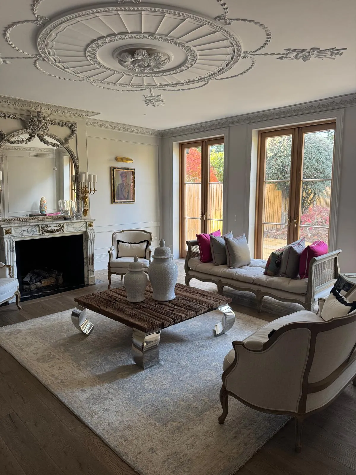 Formal drawing room with grey-beige panelling, ornate ceiling rose, marble fireplace, gilt French furniture and garden French doors
