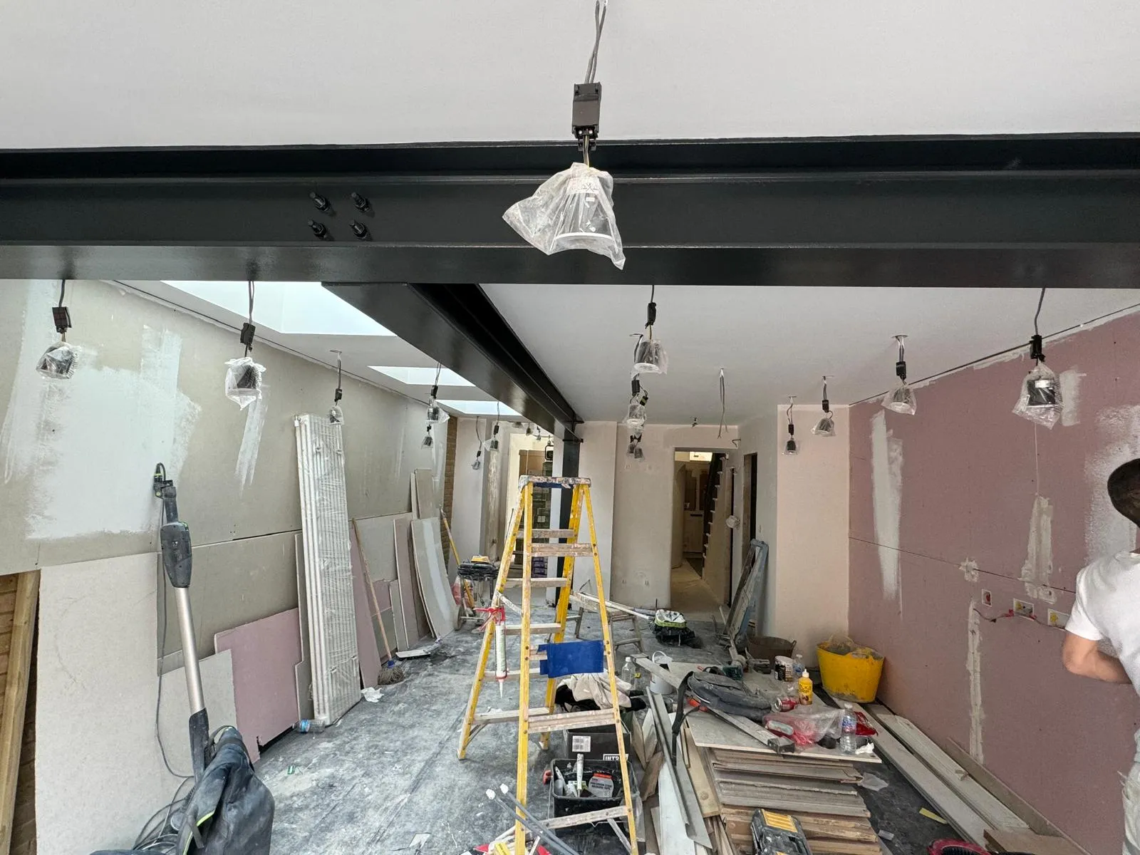Long open-plan space under construction with steel RSJ beam, plasterboard walls, skylights and construction equipment